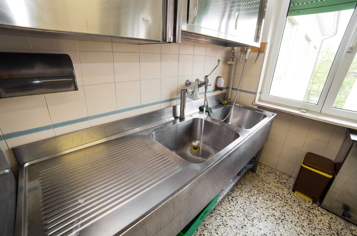 Stainless steel double-basin commercial sink with faucet running