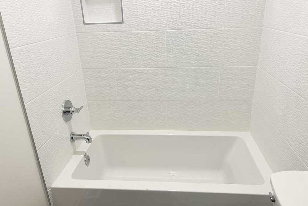 New bathtub with chrome shower valve and spout in white tile surround