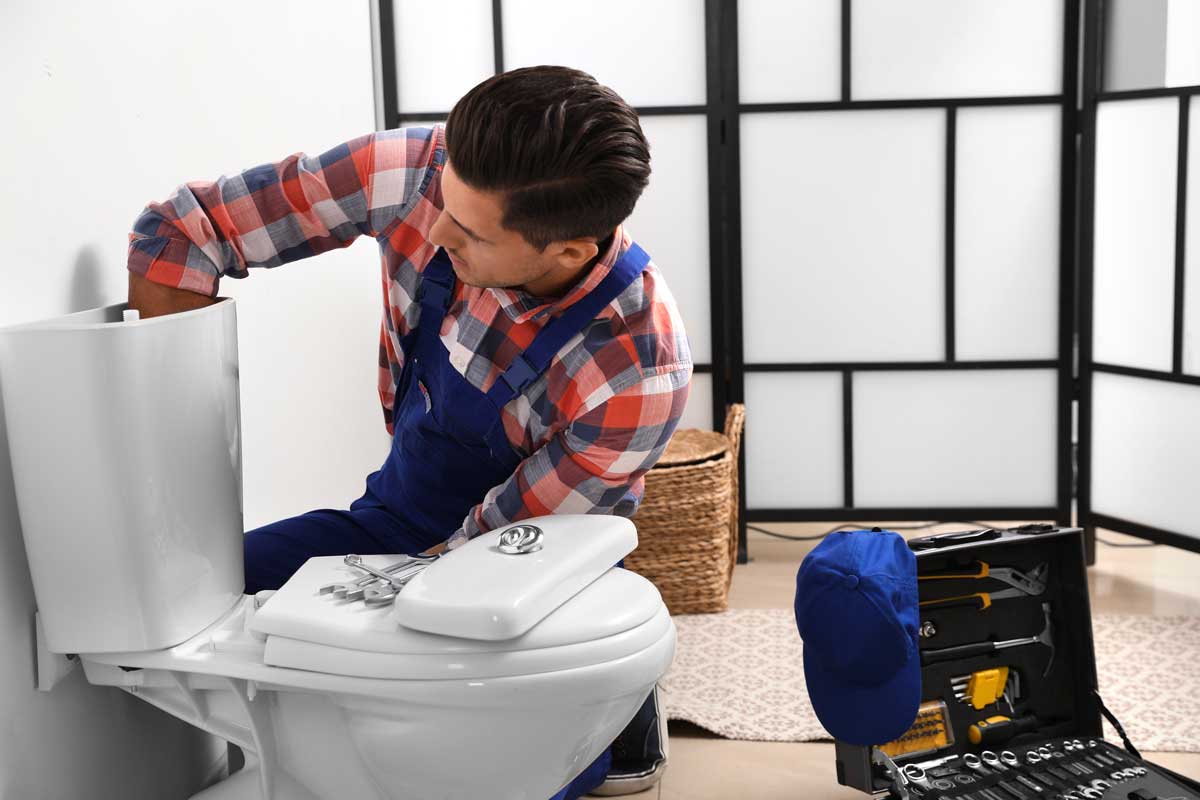 Plumber repairing a toilet tank with tools nearby